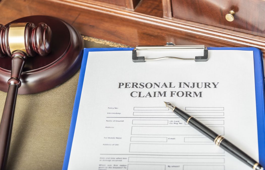 A personal injury claim form on a clipboard with a pen beside it, next to a wooden judge's gavel on a personal injury lawyer's desk.