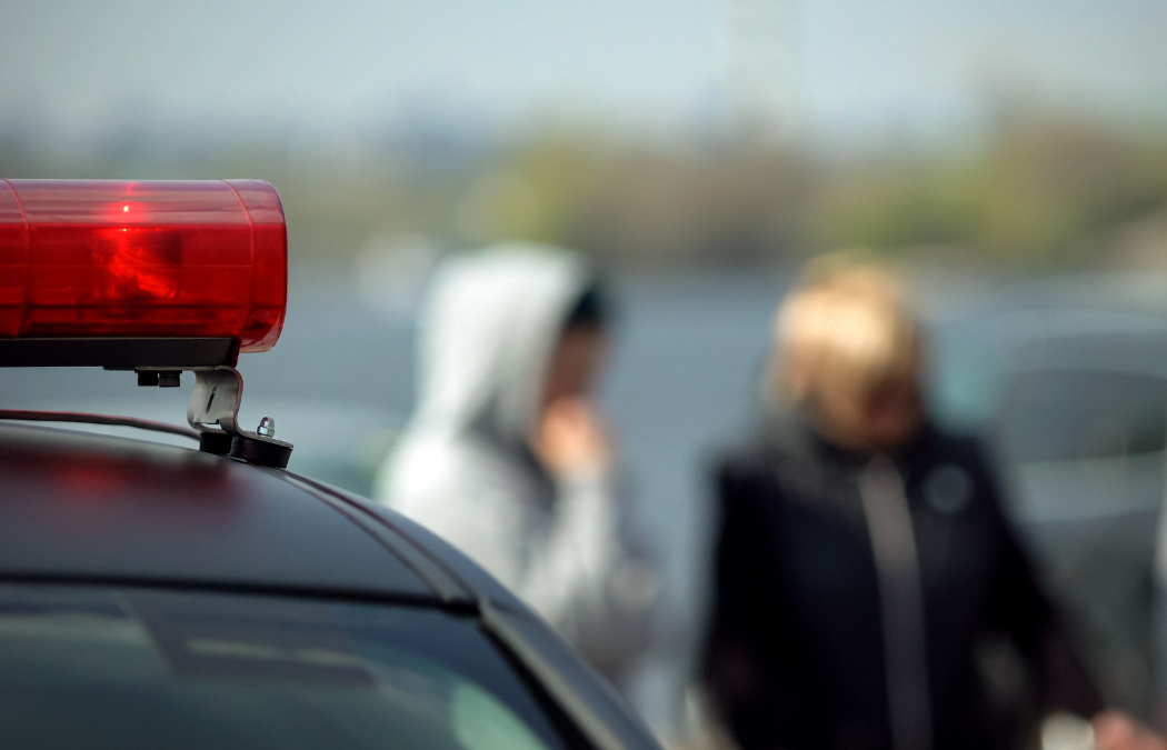 A blurred image showing two people in the background. In the foreground, a red emergency vehicle light is visible.