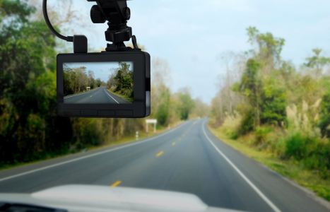 View of a dashcam recording an empty rural road with green foliage on either side.