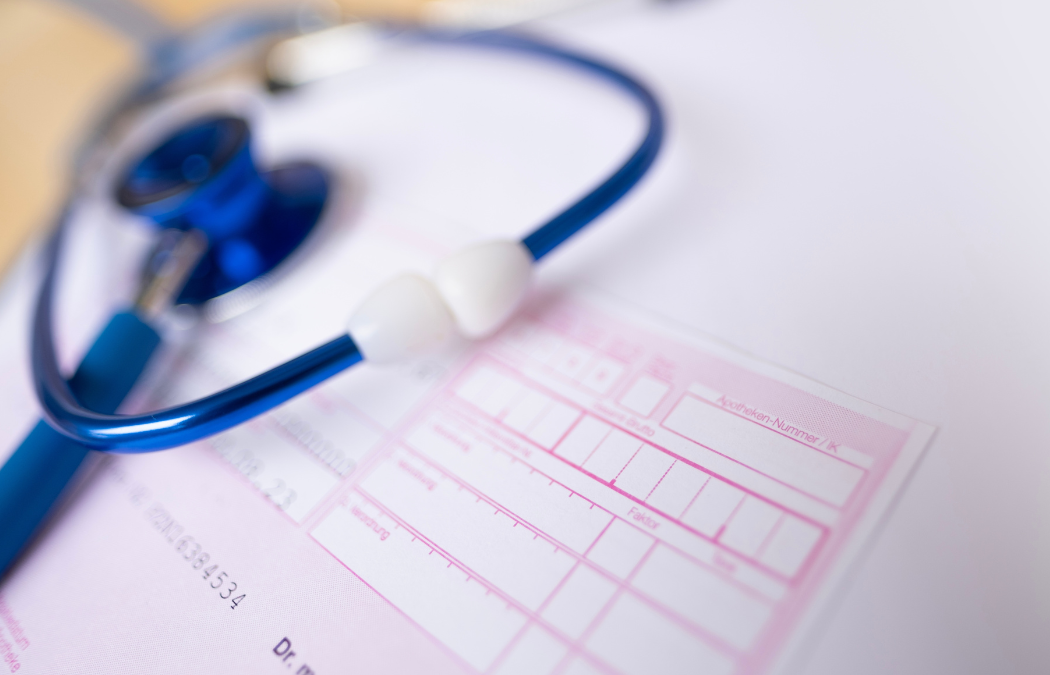 A blue stethoscope rests on a pink medical prescription pad, which is partially visible.