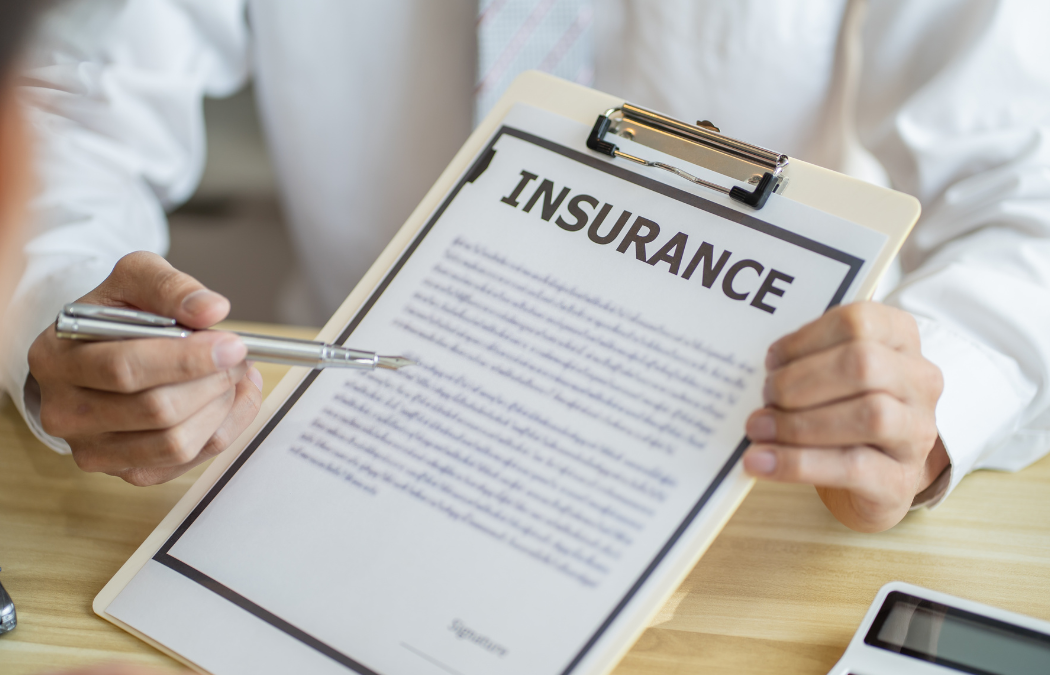 Person in a white shirt holding a clipboard with an insurance document, pointing at the text with a pen.